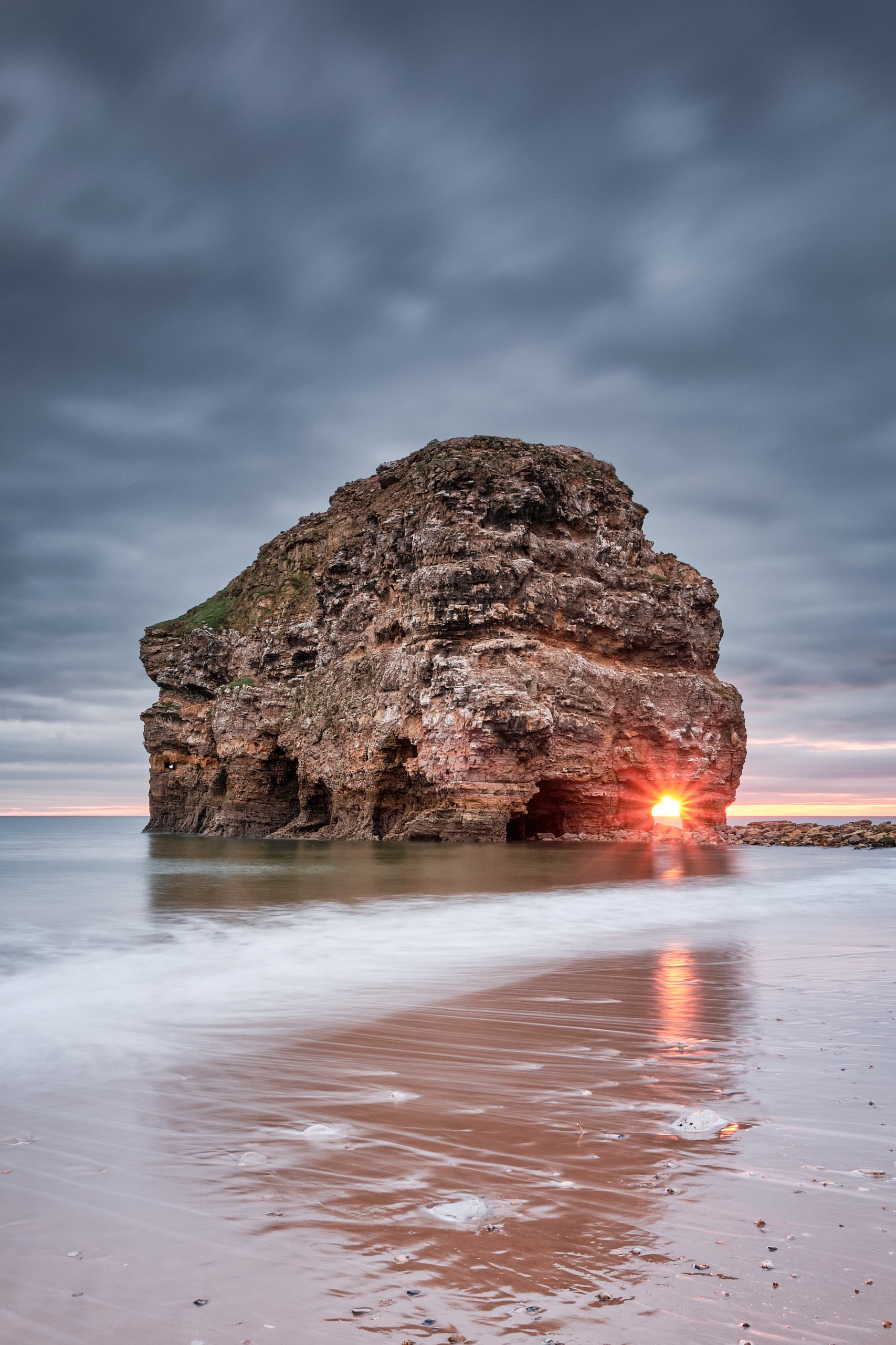 Sunrise light flaring through the rock arch at Marsden Bay