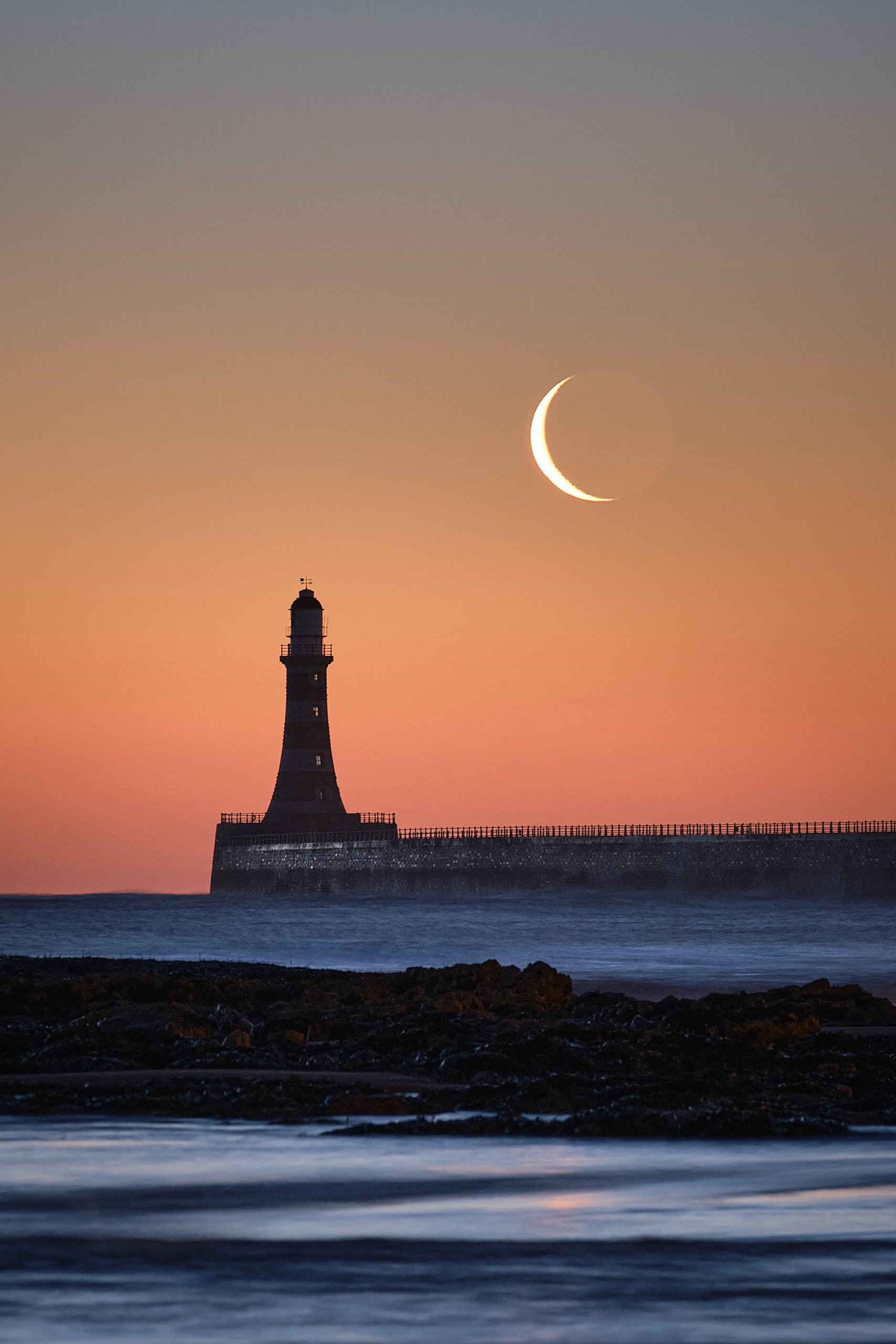 Roker Pier lighthouse under a crescent moon during blue hour